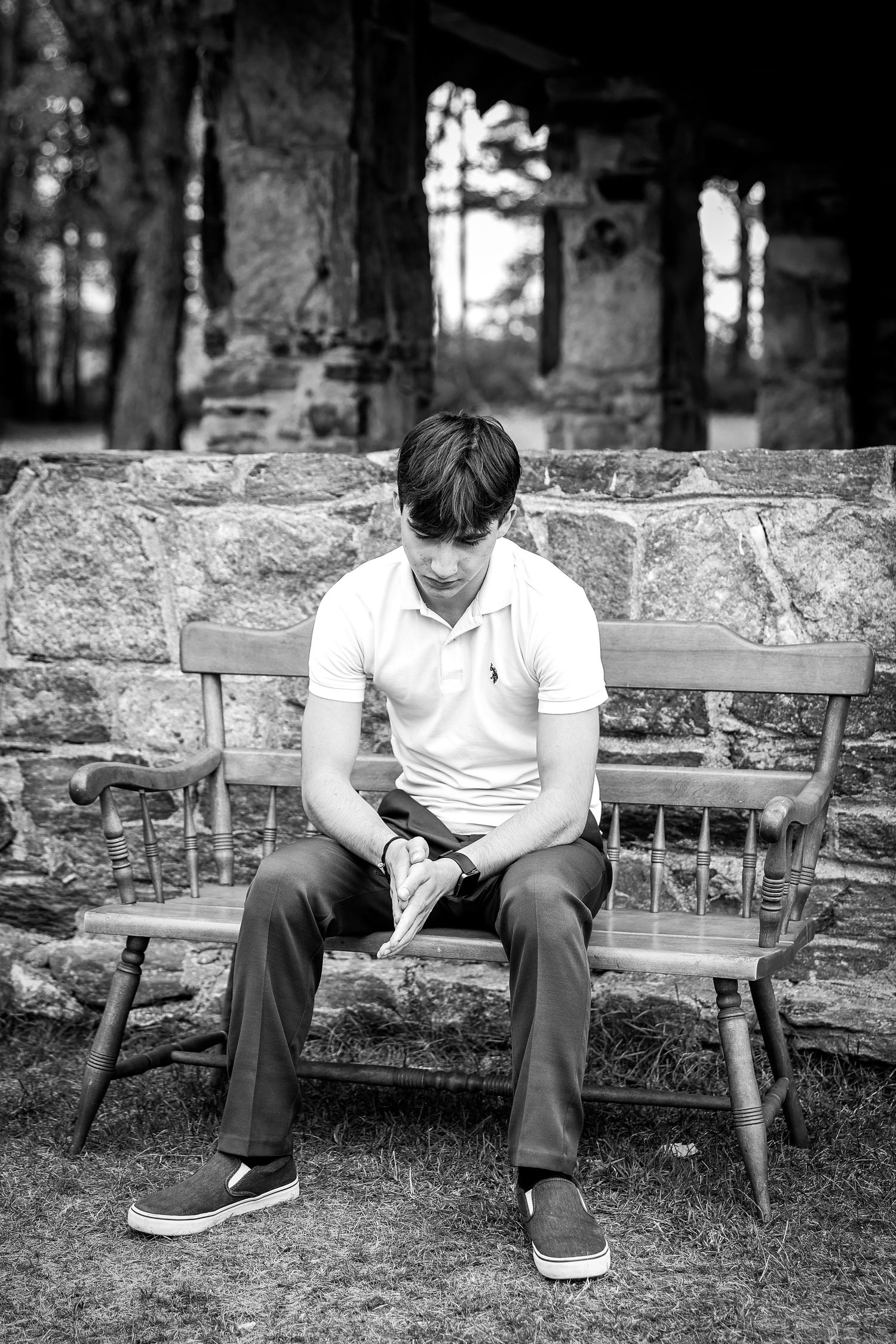 Black and white photo of a young man sitting on a wooden bench reading outdoors.