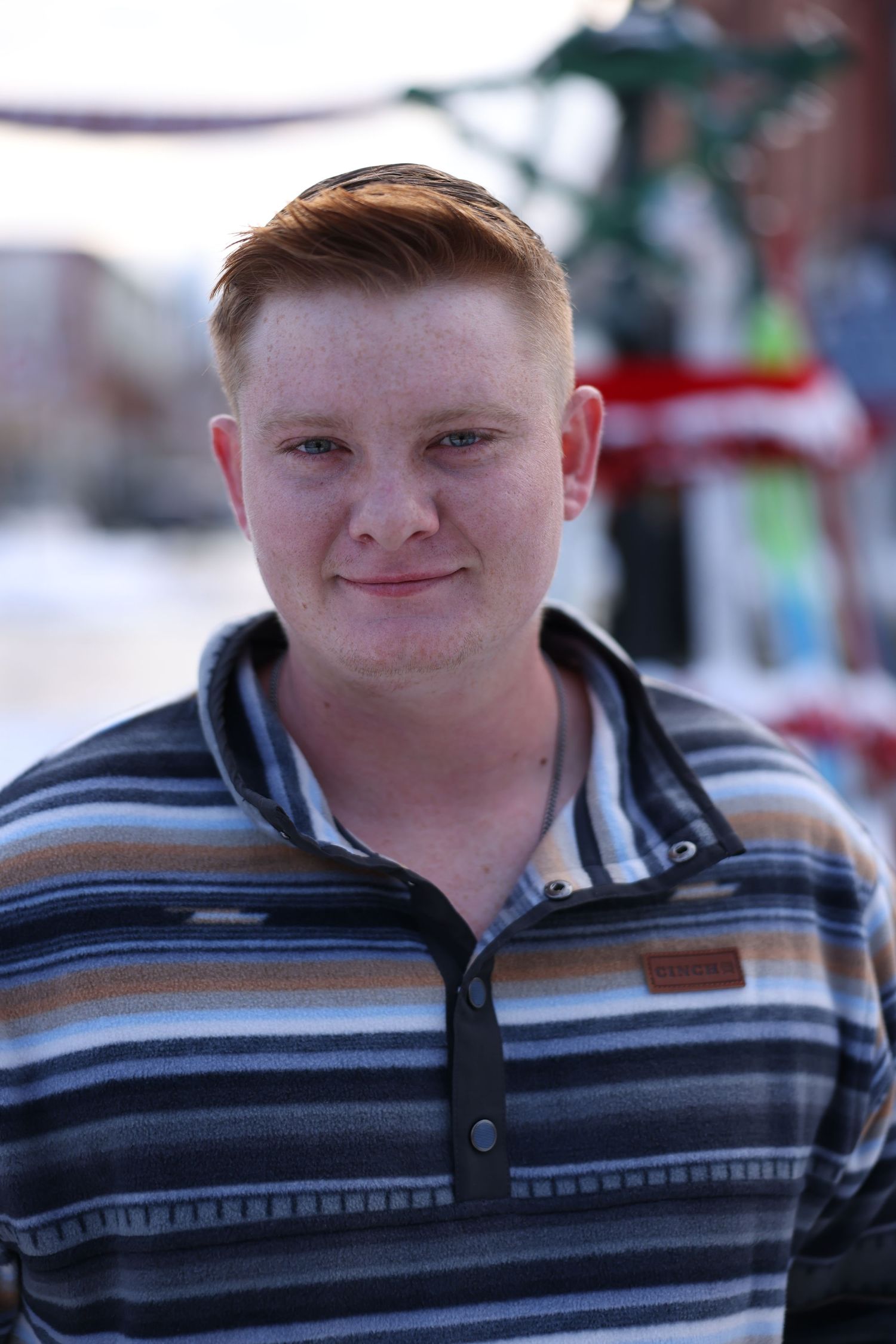 Smiling red-haired teenage boy with freckles wearing a striped pullover sweater outdoors in winter.