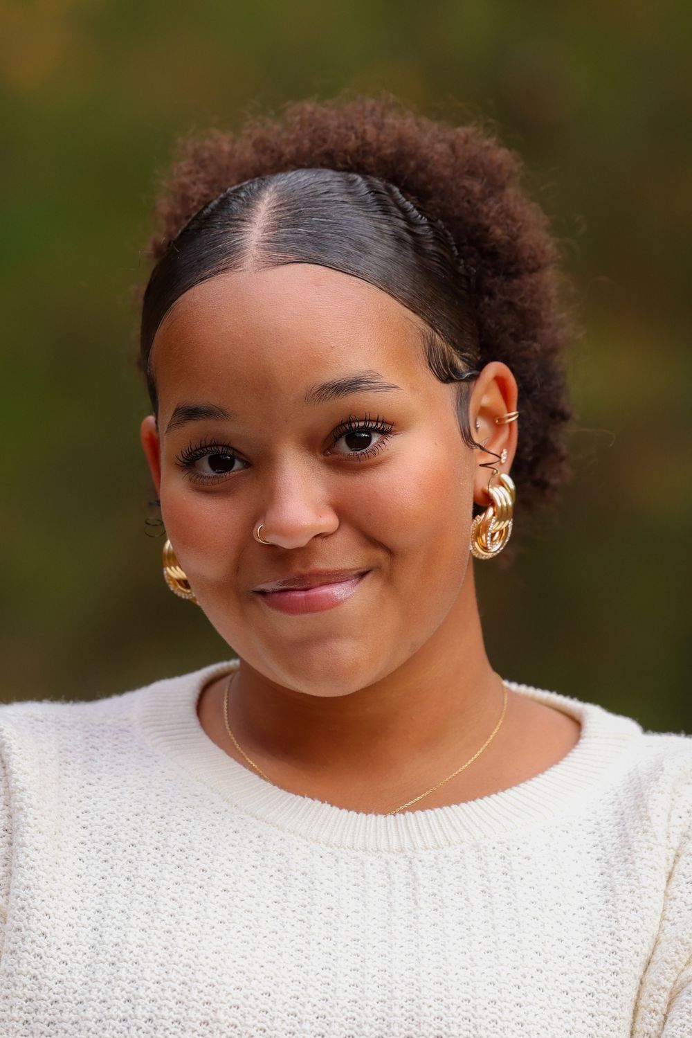 Close-up portrait of young woman with natural hair and gold earrings smiling outdoors.
