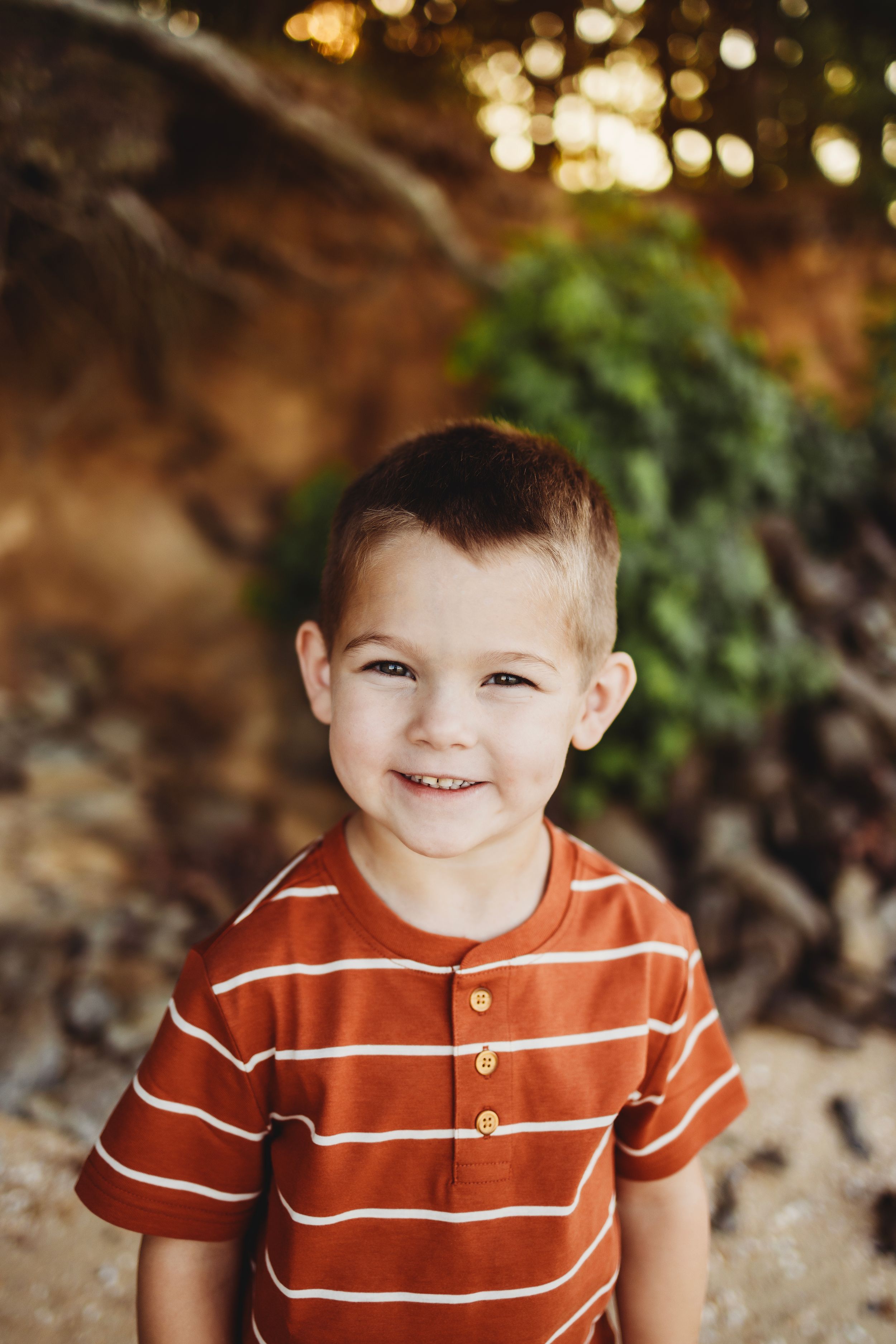 Young child in orange striped polo shirt smiles brightly outdoors.