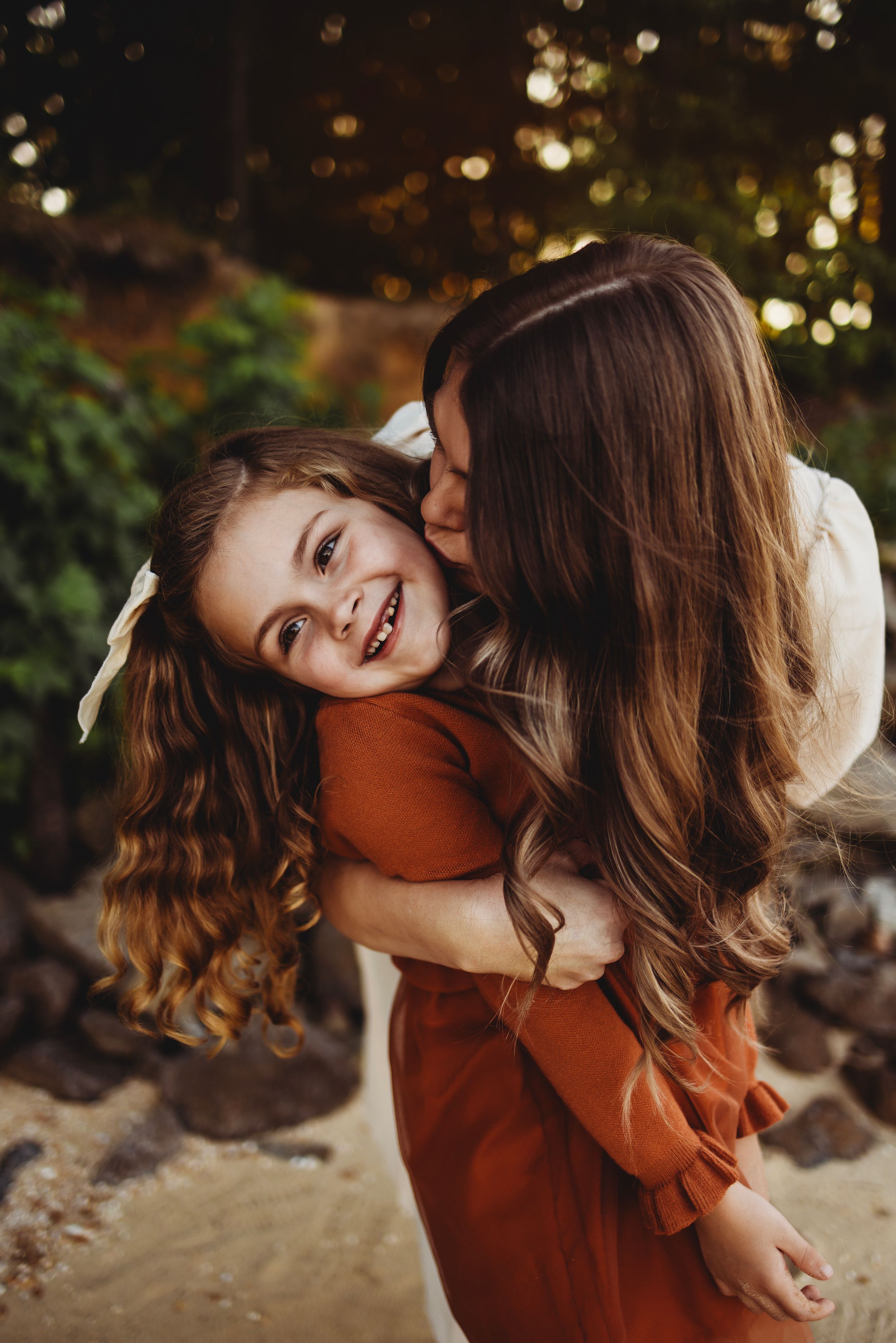 Sweet candid moment shared between parent and child in rust-colored dress against natural backdrop.