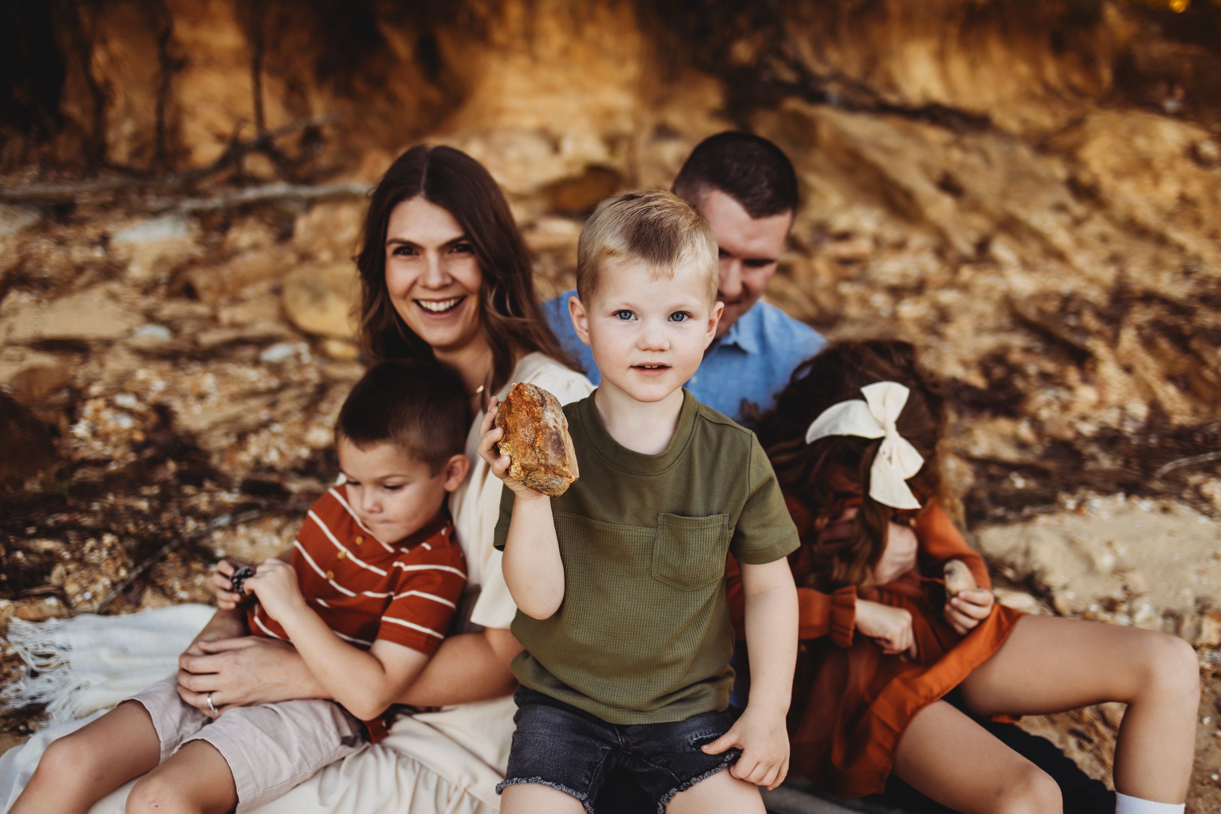 Family sitting together on rocky beach with stuffed animal toys.
