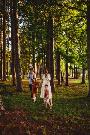 Family walking together through sunlit pine forest on nature trail.