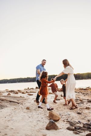 Family dancing and playing together on rocky beach at sunset.