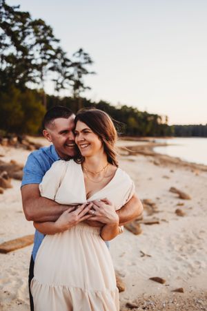 Couple sharing an intimate moment while embracing on a lakeside beach during golden hour.