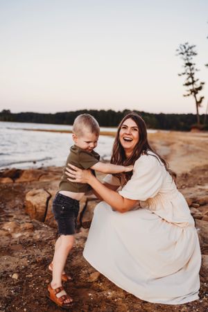 Playful moment captured between mother and child on rocky beach during sunset.