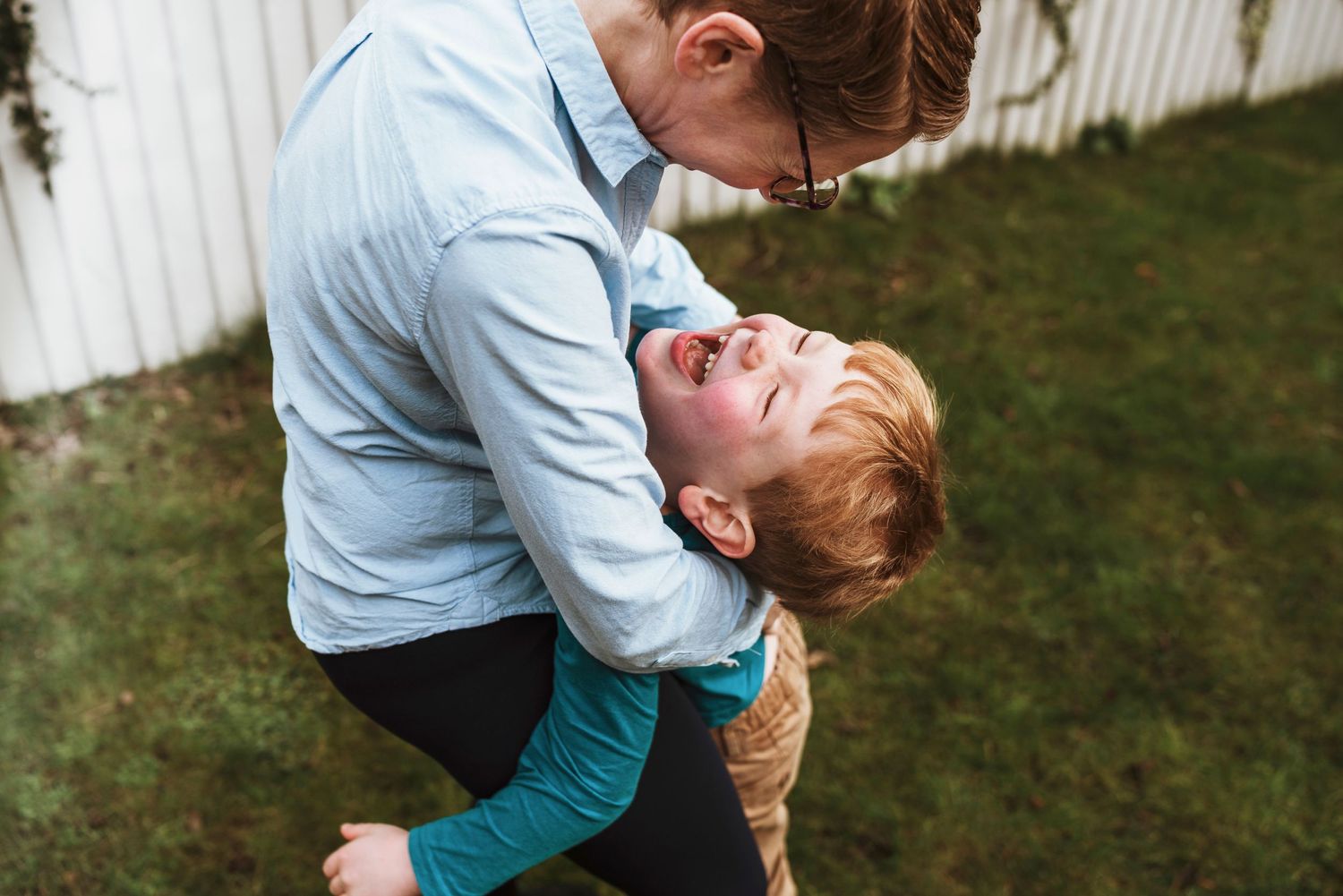 Playful moment captured in a backyard with white picket fence background.