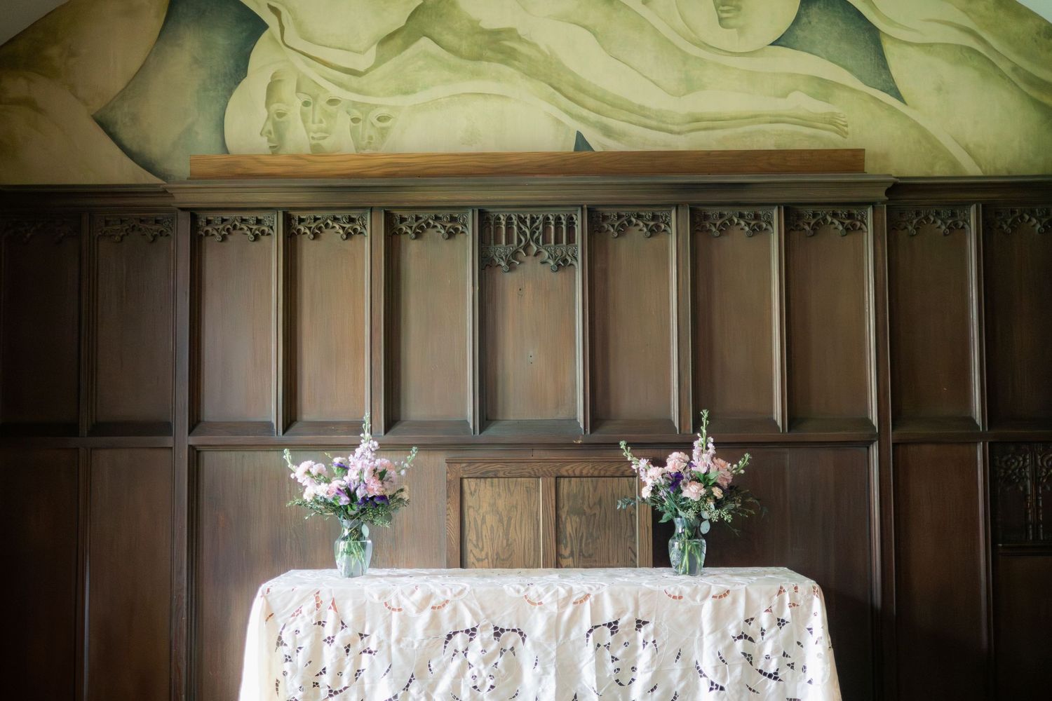 A reception table with lace tablecloth and floral arrangements against dark wood paneled walls.