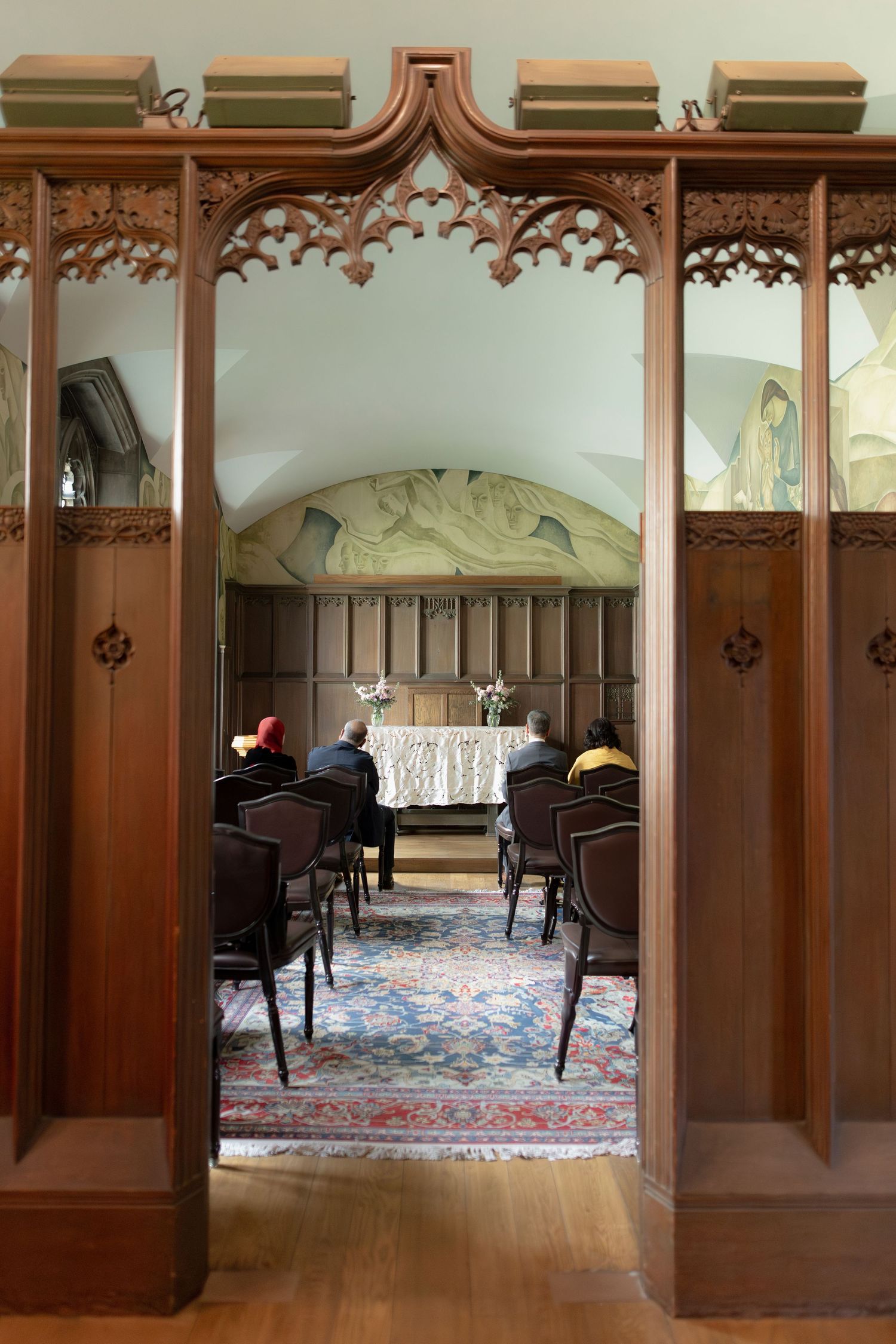 An ornate wooden archway leading into a chapel with stained glass and wood paneling.