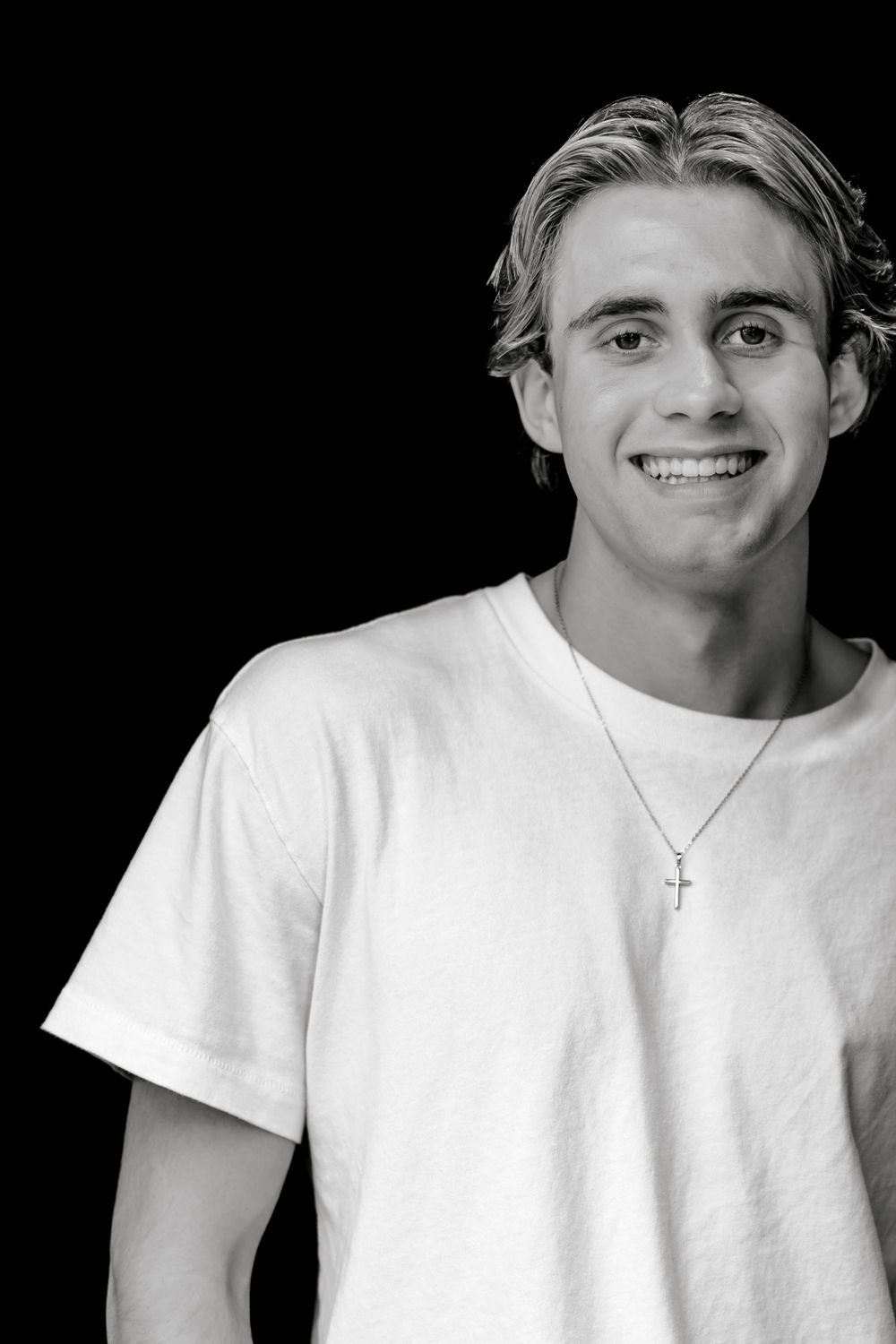Black and white portrait of smiling young man wearing white tee and cross necklace.