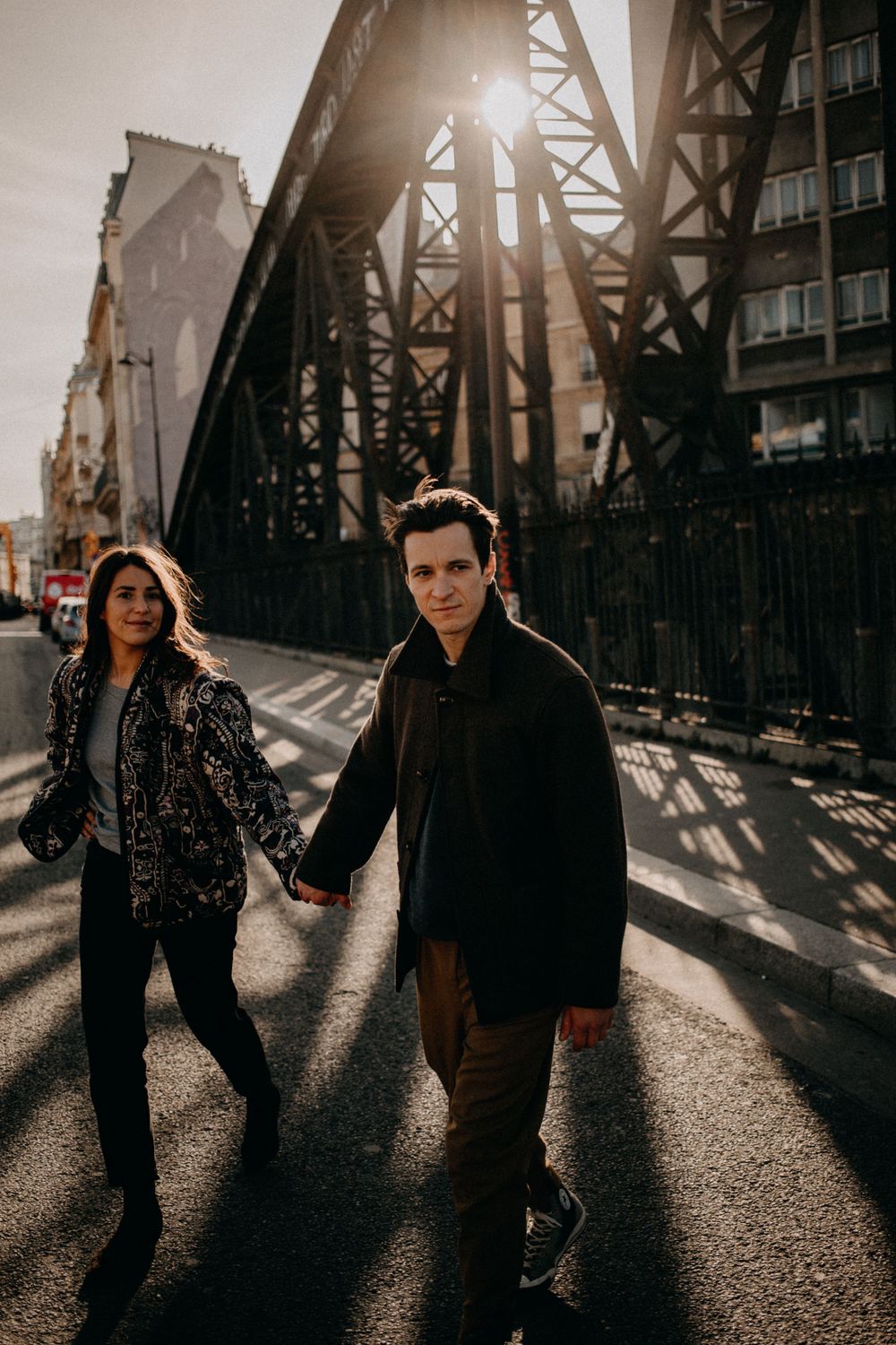 A couple walking beneath a large bridge structure during golden hour.