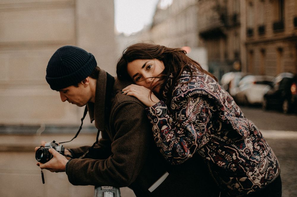 A couple sharing an intimate moment while looking at a camera on a city street.