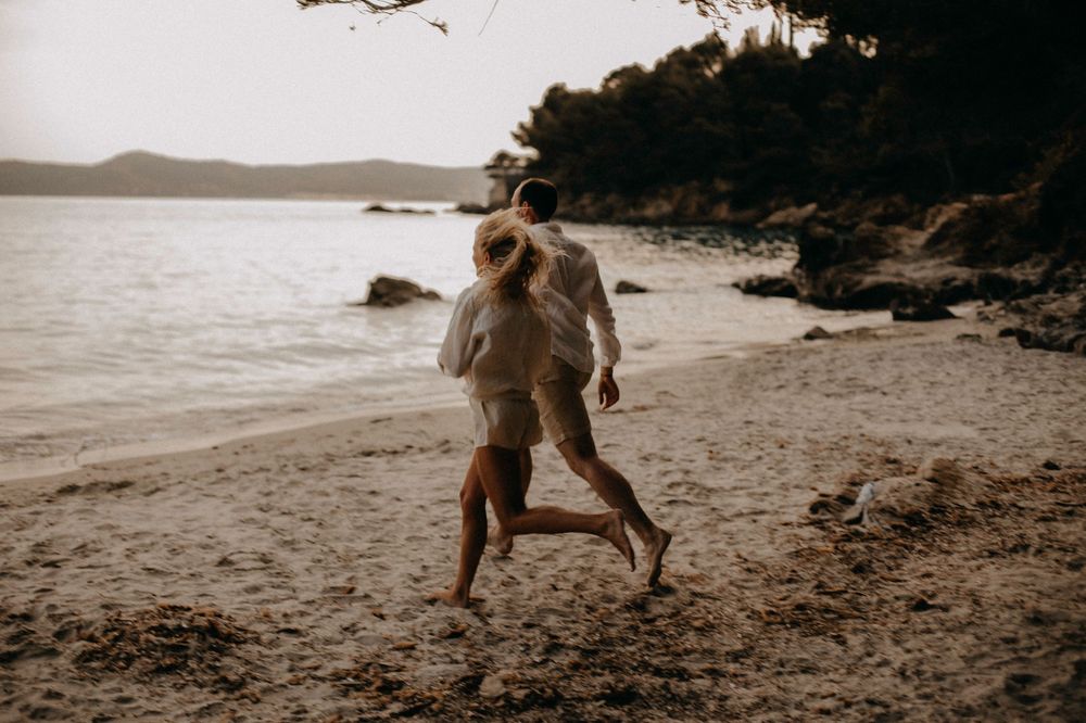Couple running along rocky beach shore in sepia tones.