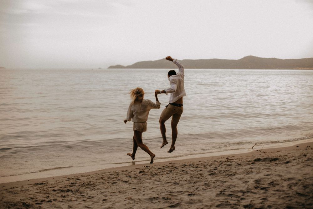 Two people jumping playfully on beach at sunset in black and white.