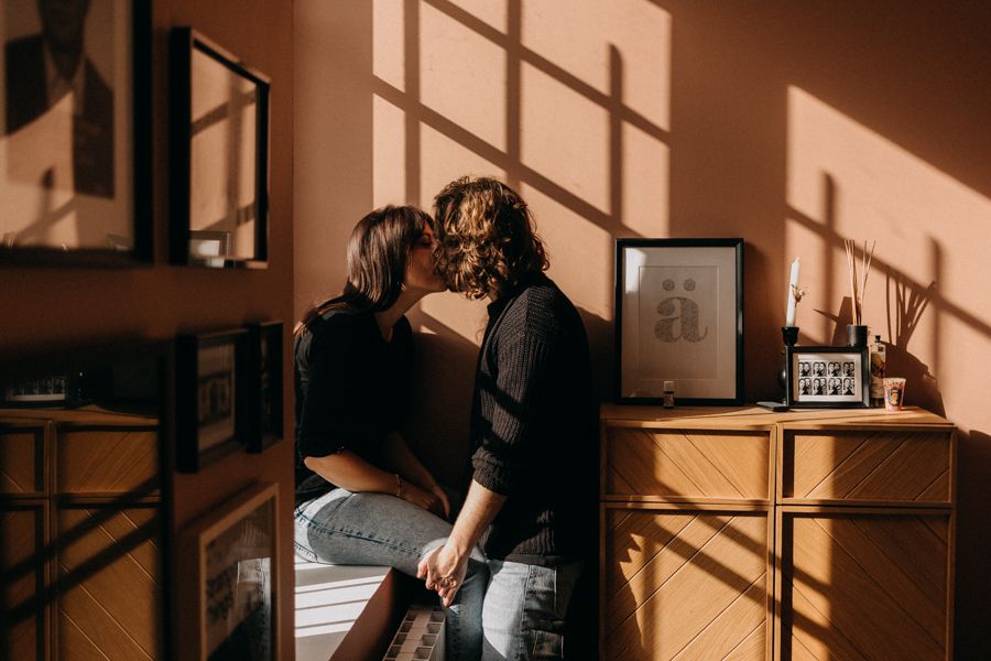 Couple sharing an intimate moment in a sunlit room with window shadows on the wall.