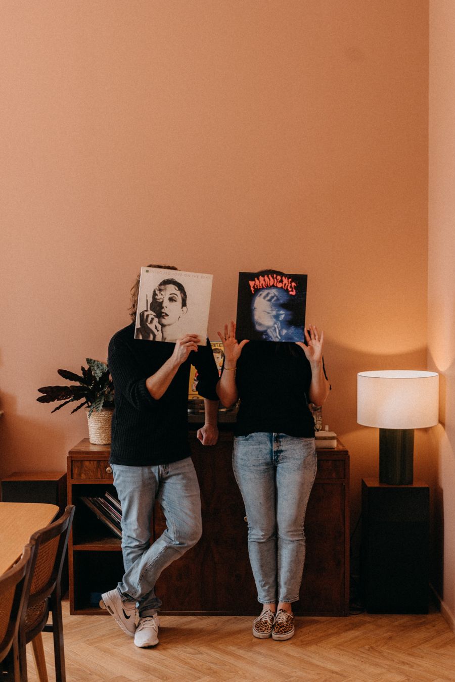 Two people holding vinyl records in front of their faces against peachy wall.