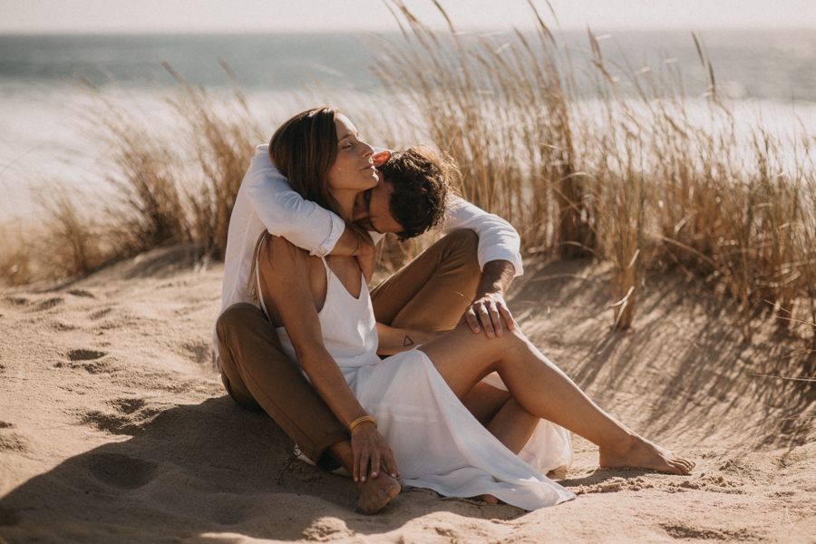 Couple embracing on sandy beach dunes during golden hour.