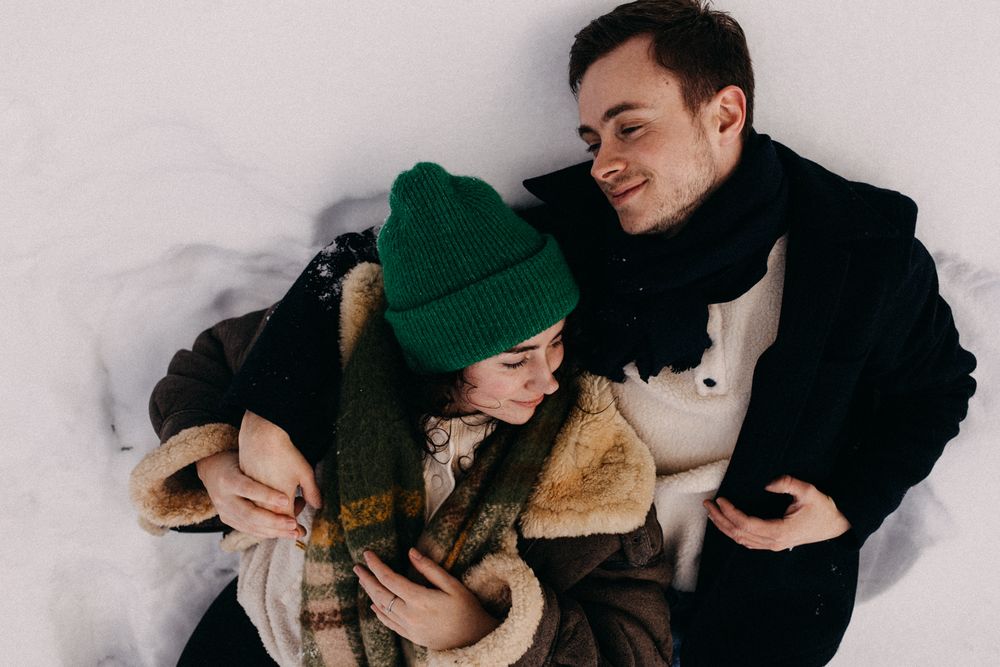 A cozy winter moment of two people snuggled together in the snow wearing warm clothing.