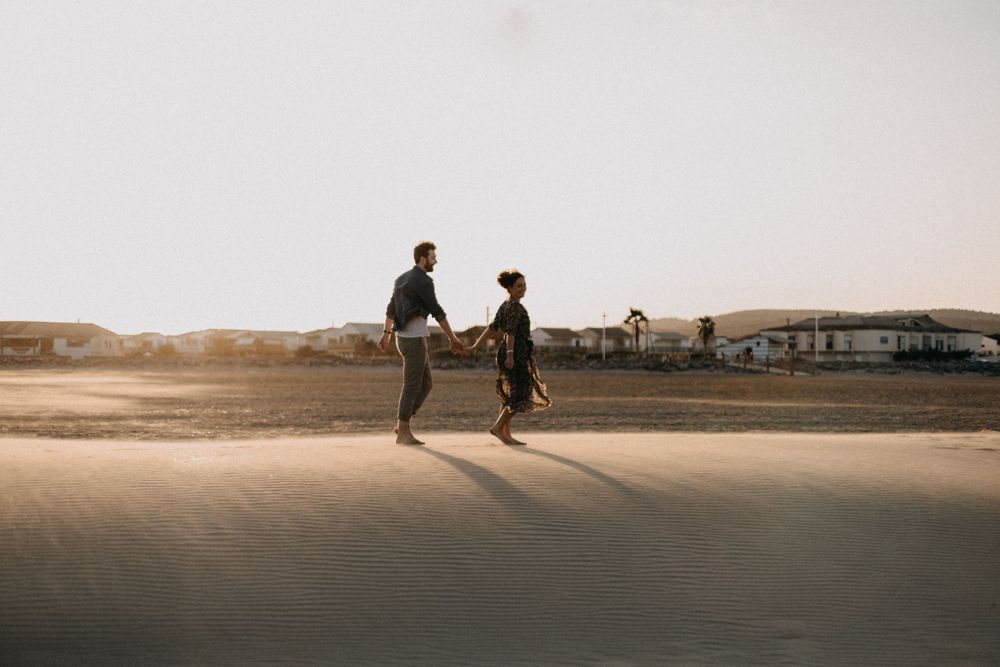 Two silhouettes running together on a beach at sunset.
