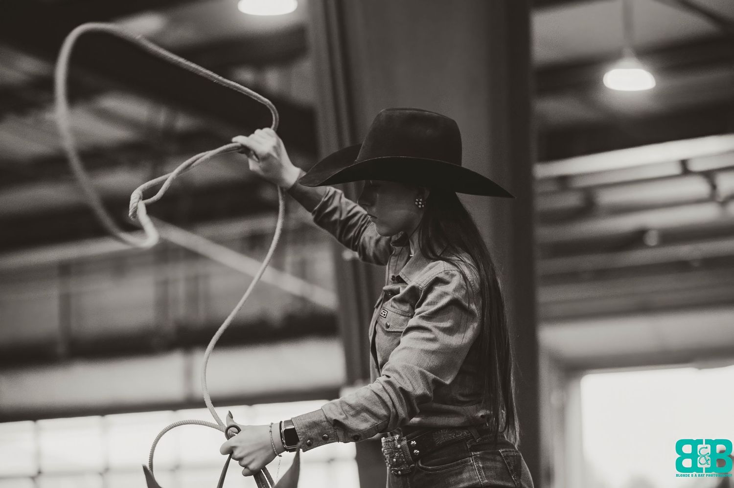 Black and white photo of cowboys preparing equipment at an indoor arena.