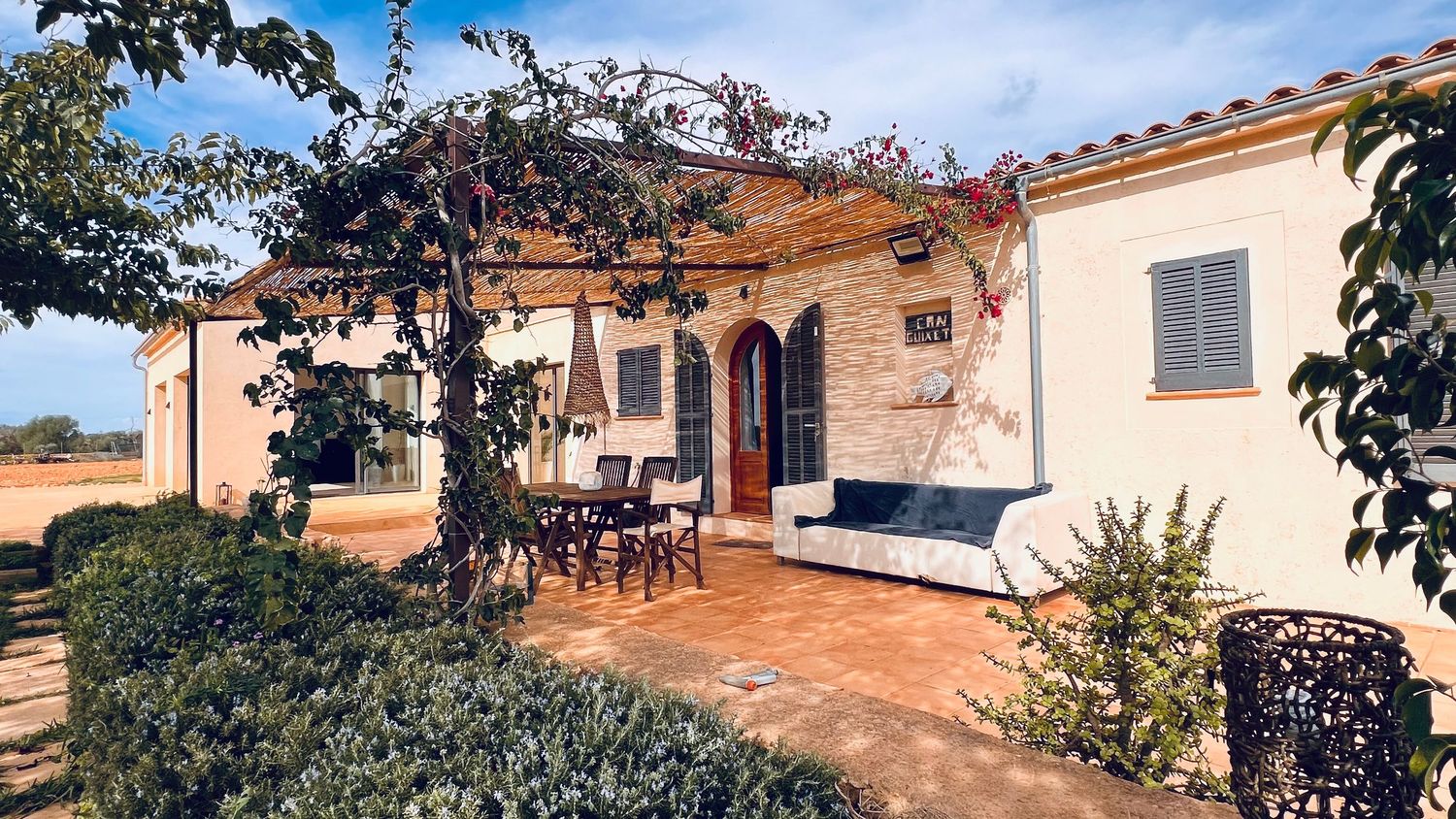 Rustic outdoor dining area under a wooden pergola with Mediterranean landscaping.