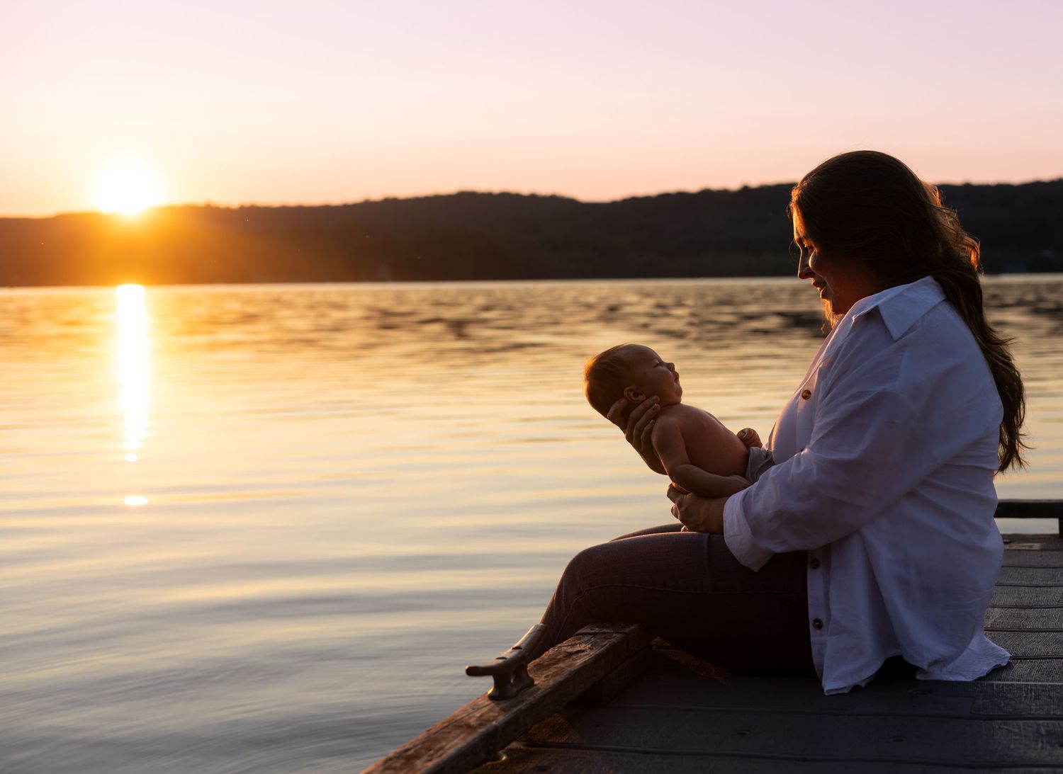 Silhouettes of couple sitting by lake during dramatic sunset.