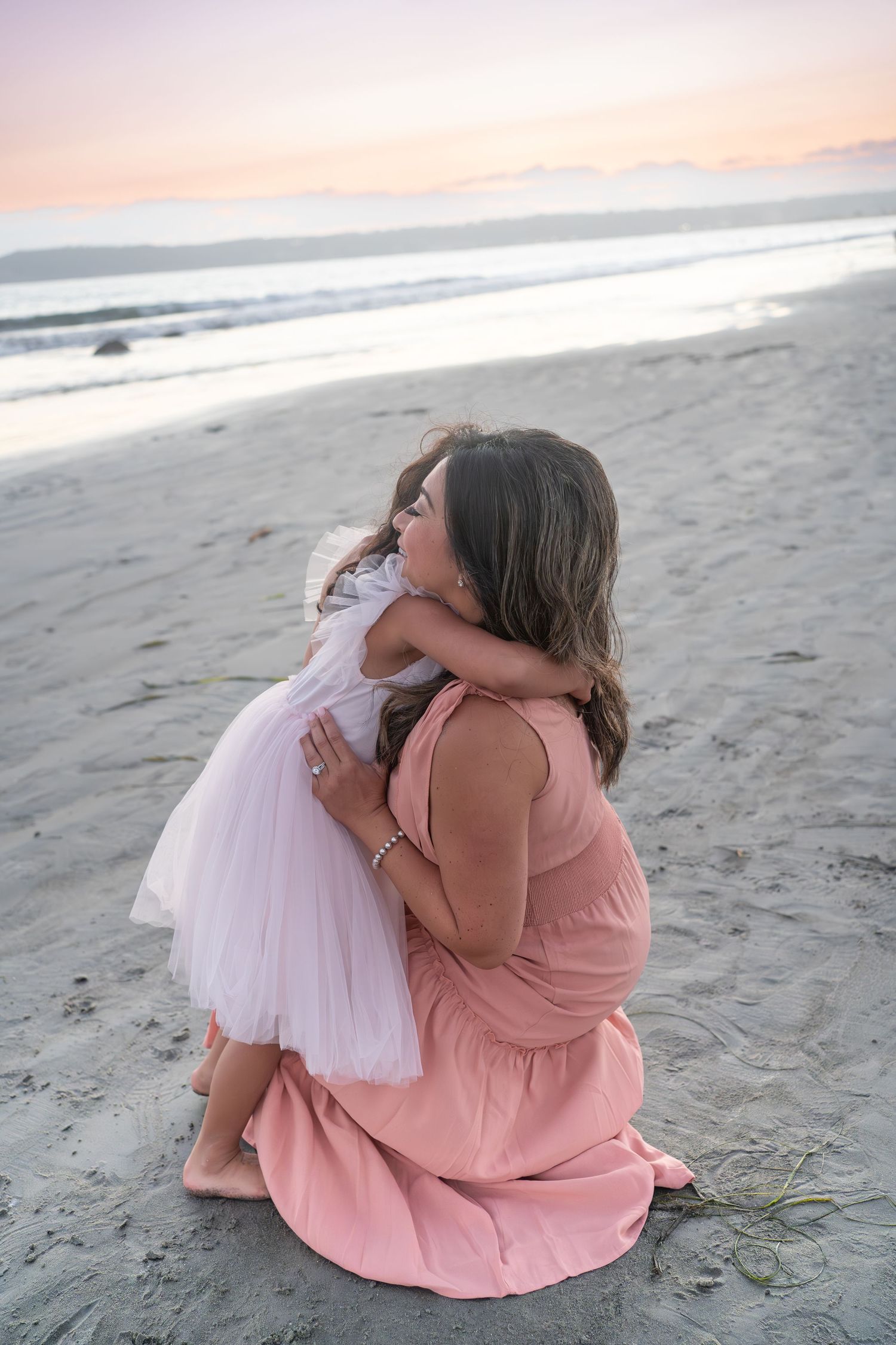 A tender moment shared between two figures in pink and white dresses on a serene beach at sunset.