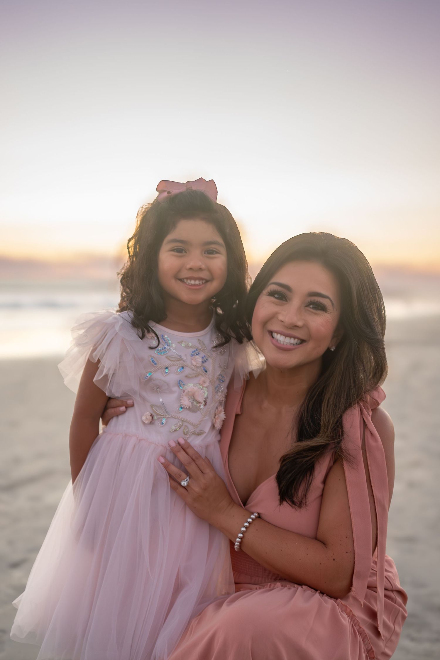A sweet moment captured at sunset on the beach with two people wearing matching pink outfits.