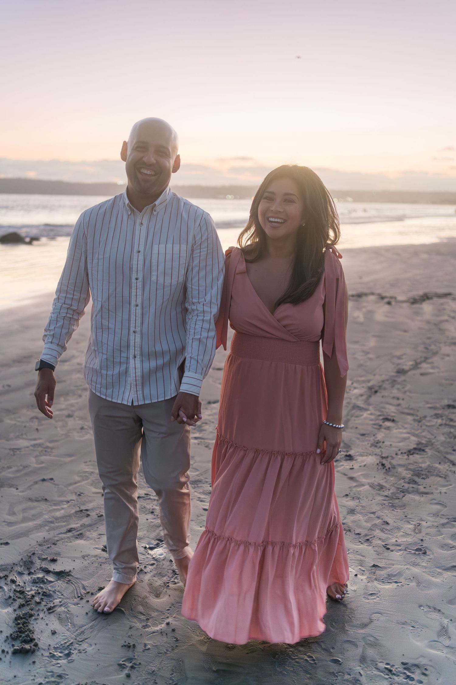 A couple walks together on a sandy beach at sunset, sharing laughter and smiles in a romantic moment.
