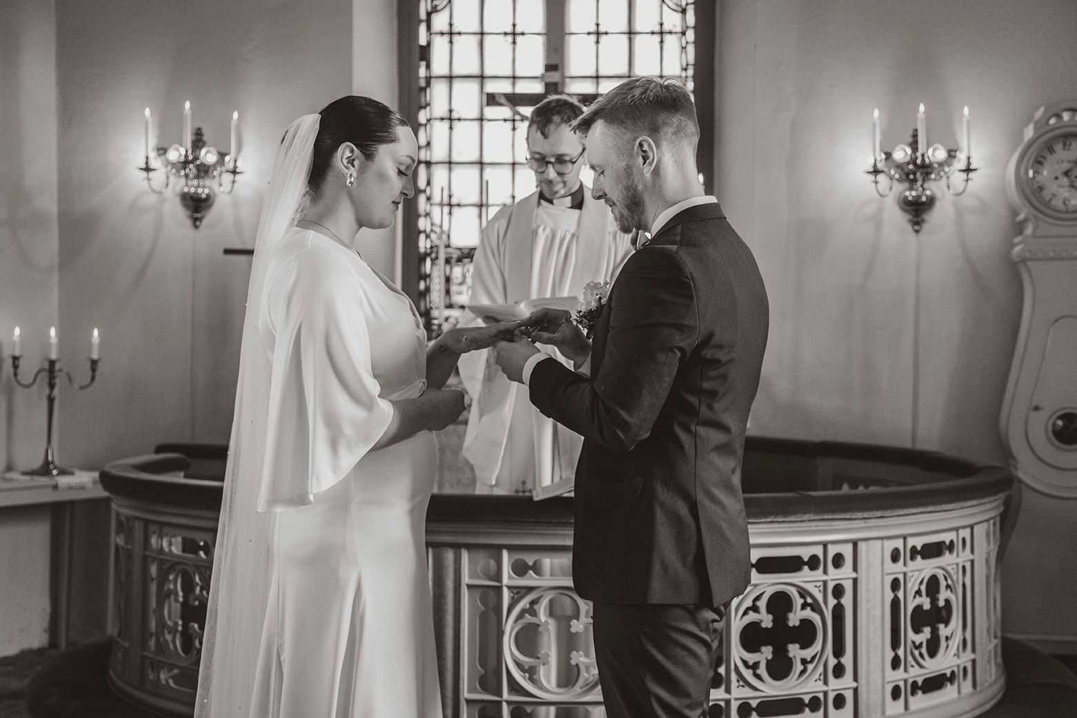 A couple exchanges rings during an intimate wedding ceremony in a chapel with candelabras and ornate details.