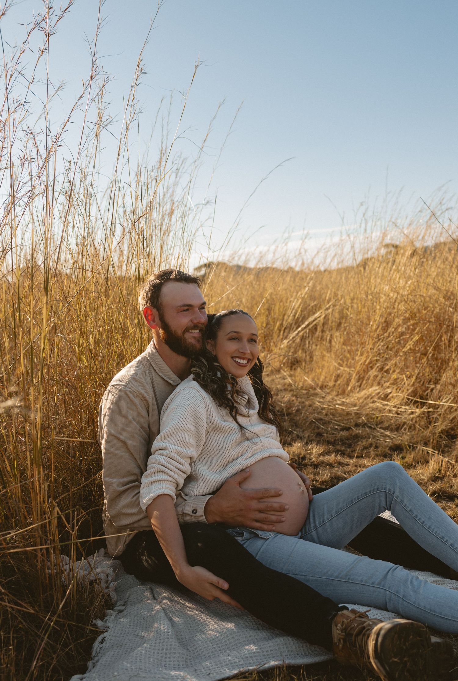 A couple lounges together in golden wheat fields at sunset on a cozy blanket, showing intimate moments of connection.