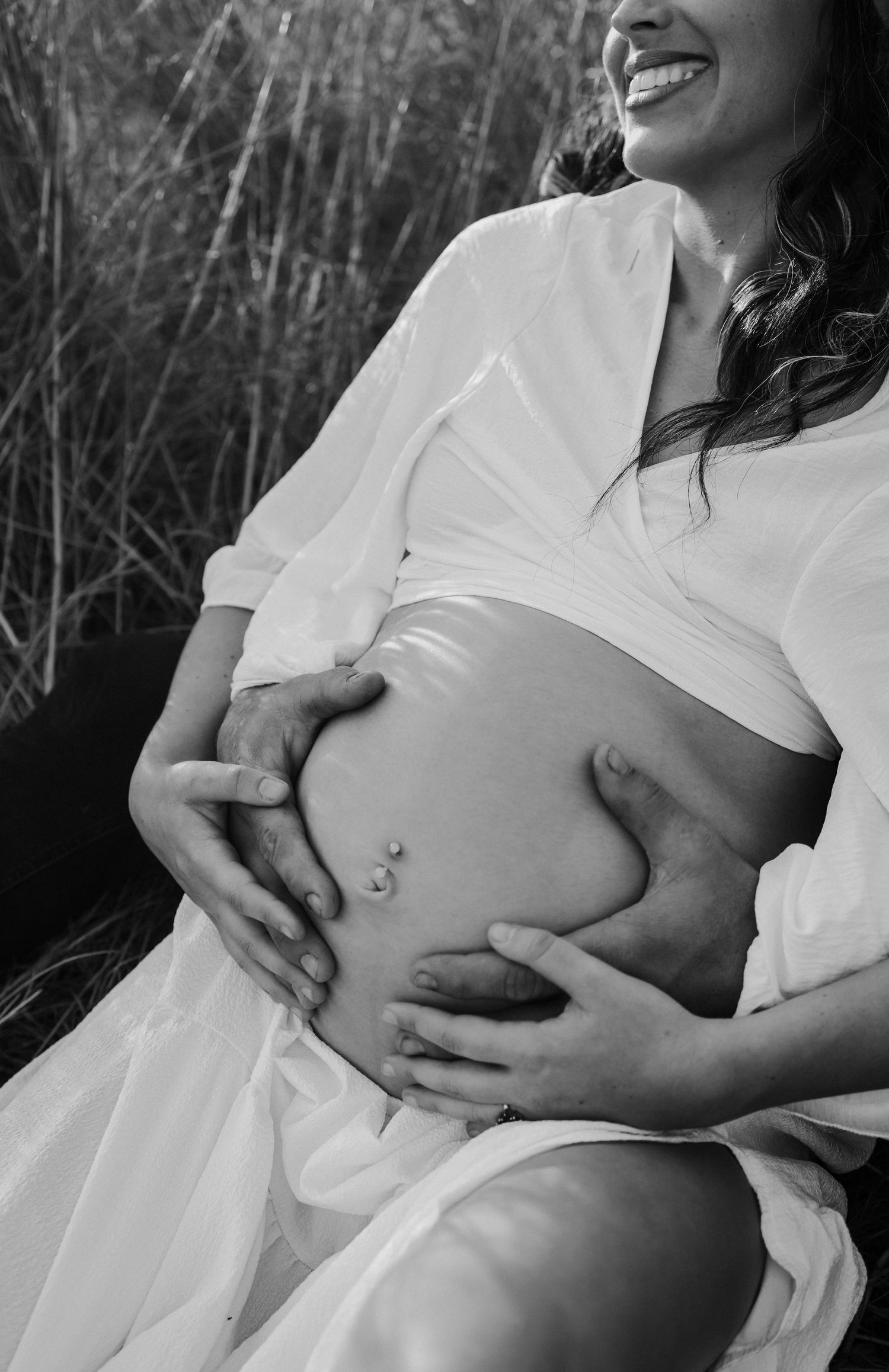 A black and white maternity photo showing a pregnant belly being gently cradled in a natural outdoor setting.