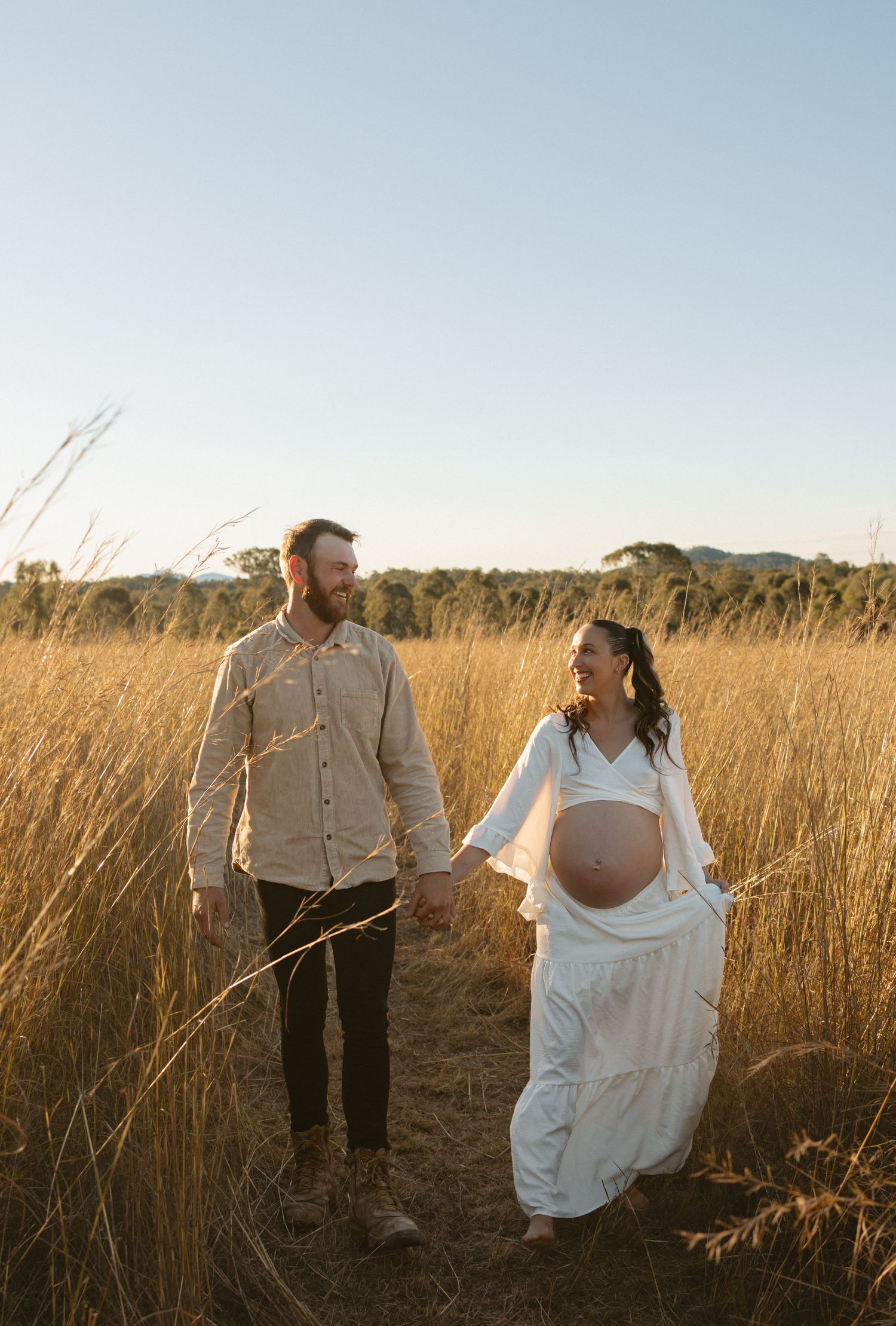 A couple stands together in a golden wheat field at sunset, sharing an intimate moment in nature.