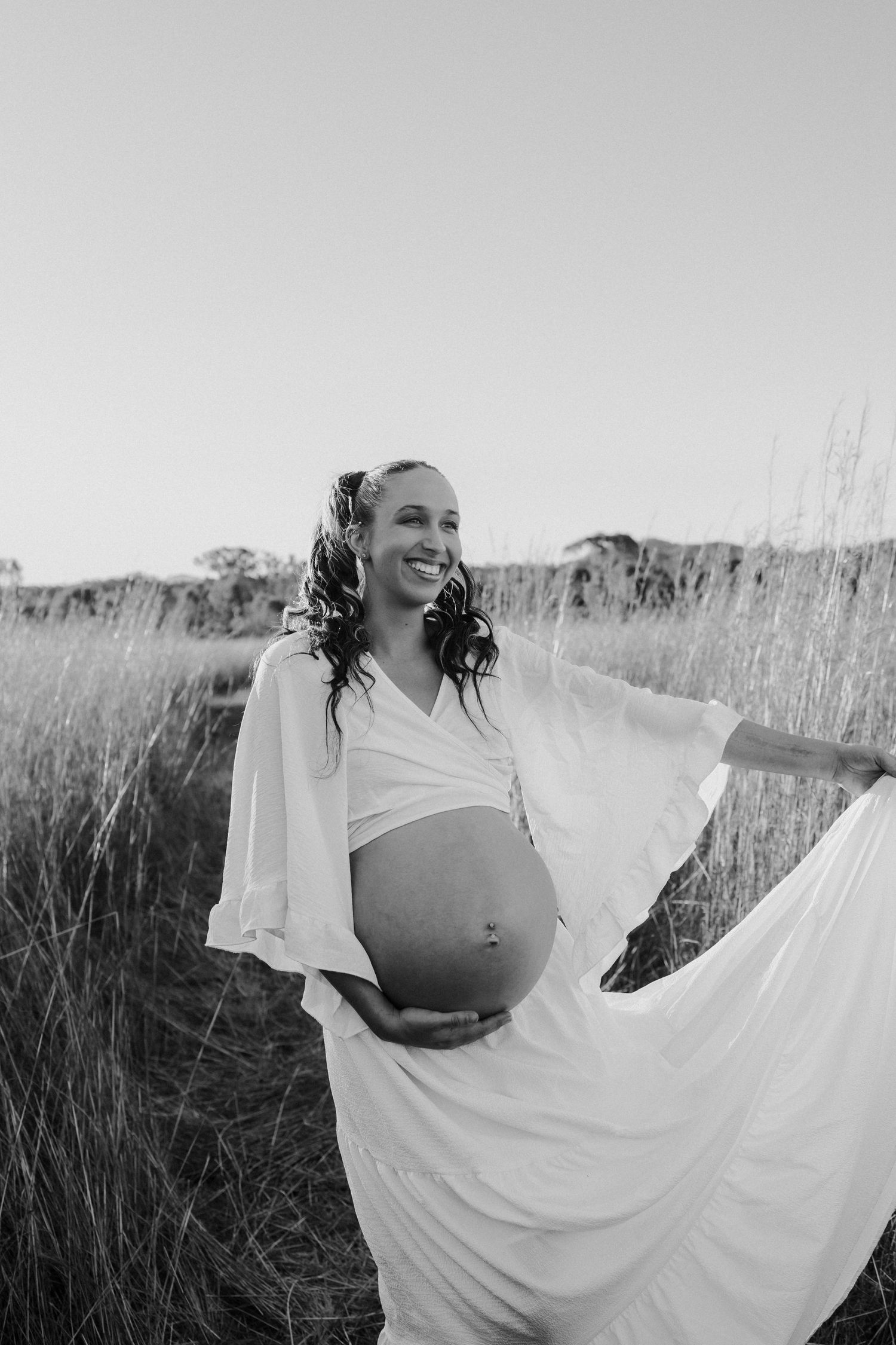 Black and white images depict a figure in a flowing white dress twirling through tall grassland at sunset.