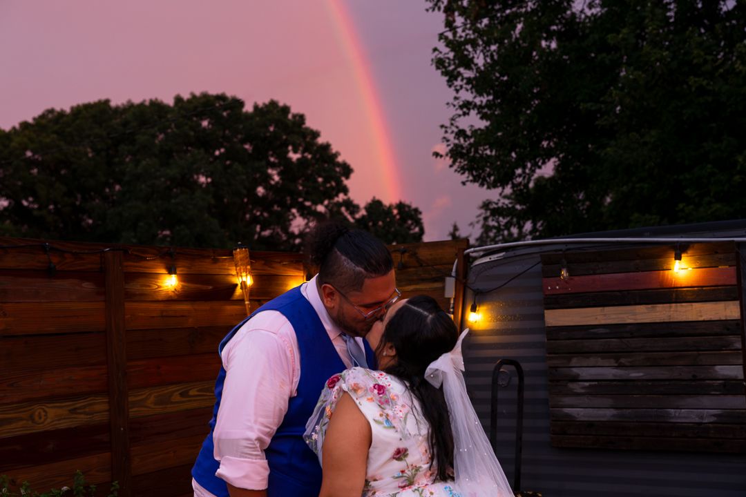 A couple shares their first kiss under a floral arch during an outdoor wedding ceremony.
