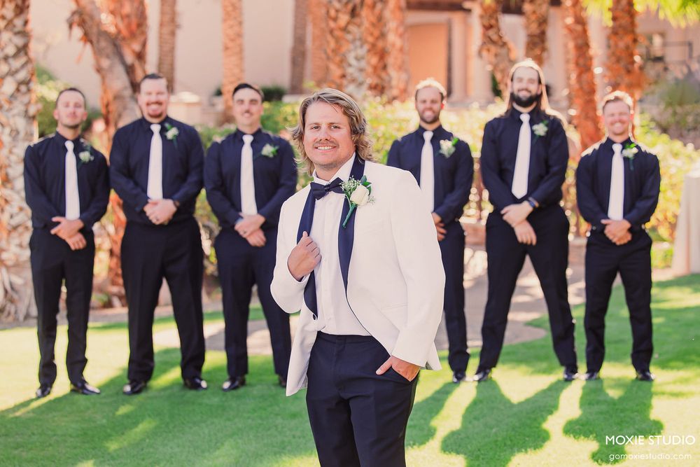 Wedding party group photo with groomsmen in formal attire against a natural backdrop.