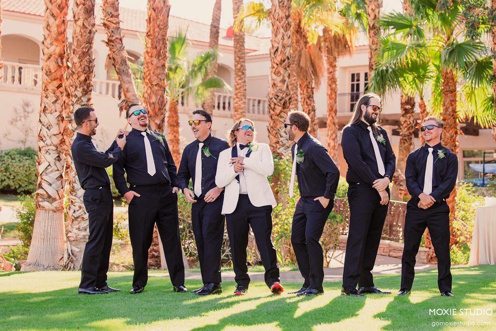 Groomsmen posing playfully in a line among palm trees at sunset.