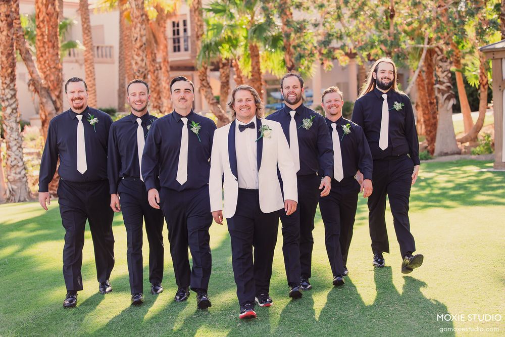 Wedding party in navy suits and white shirts posing outdoors against autumn foliage.