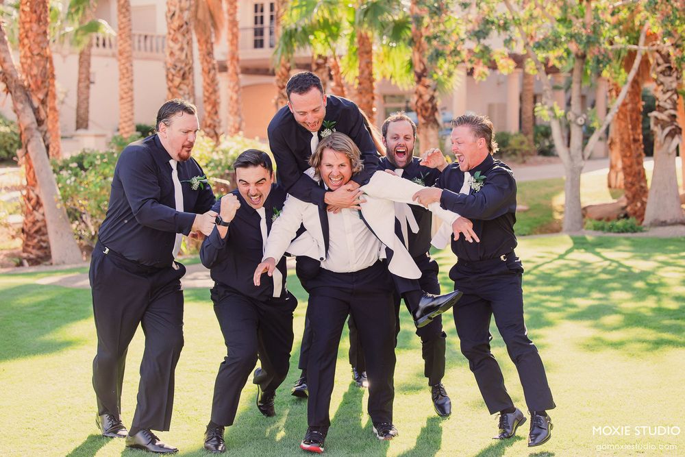 Groomsmen perform a synchronized jumping pose outdoors in formal attire during a wedding photoshoot.