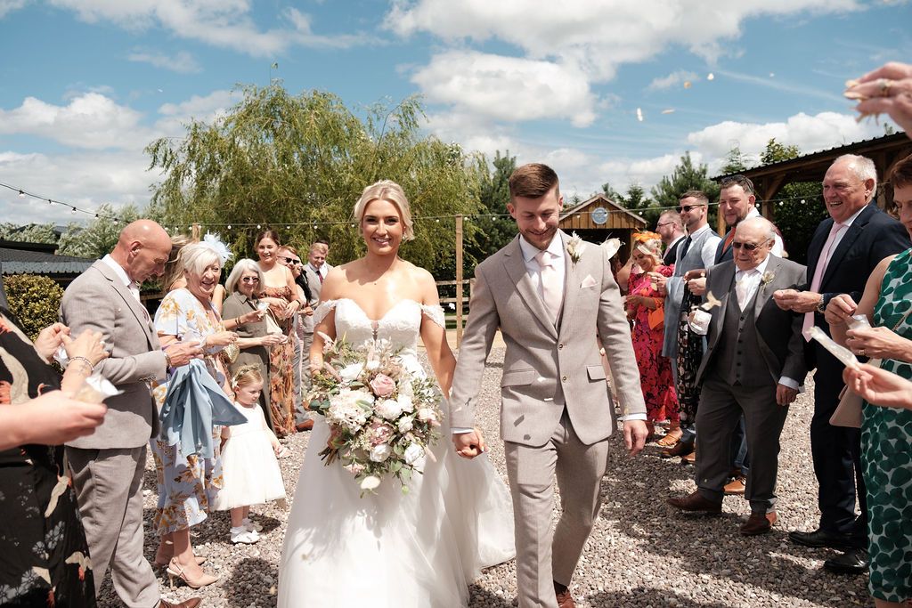 Bride and groom walking hand in hand at Coton House Farm wedding venue, surrounded by guests tossing confetti outdoors.