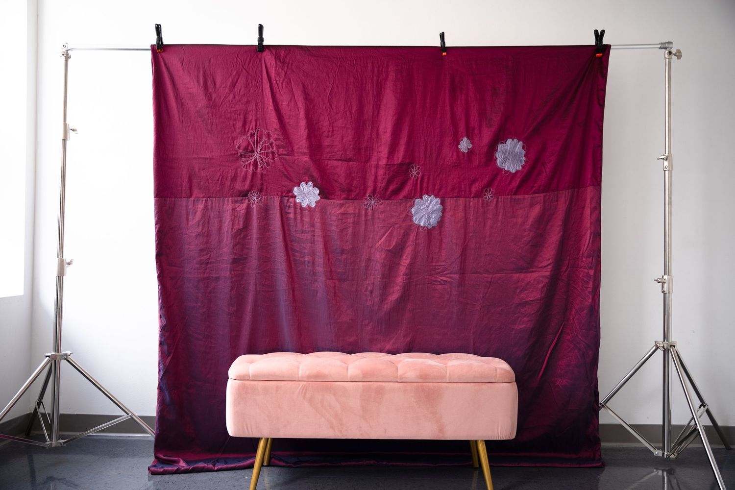Photography studio setup with burgundy backdrop and pink ottoman.