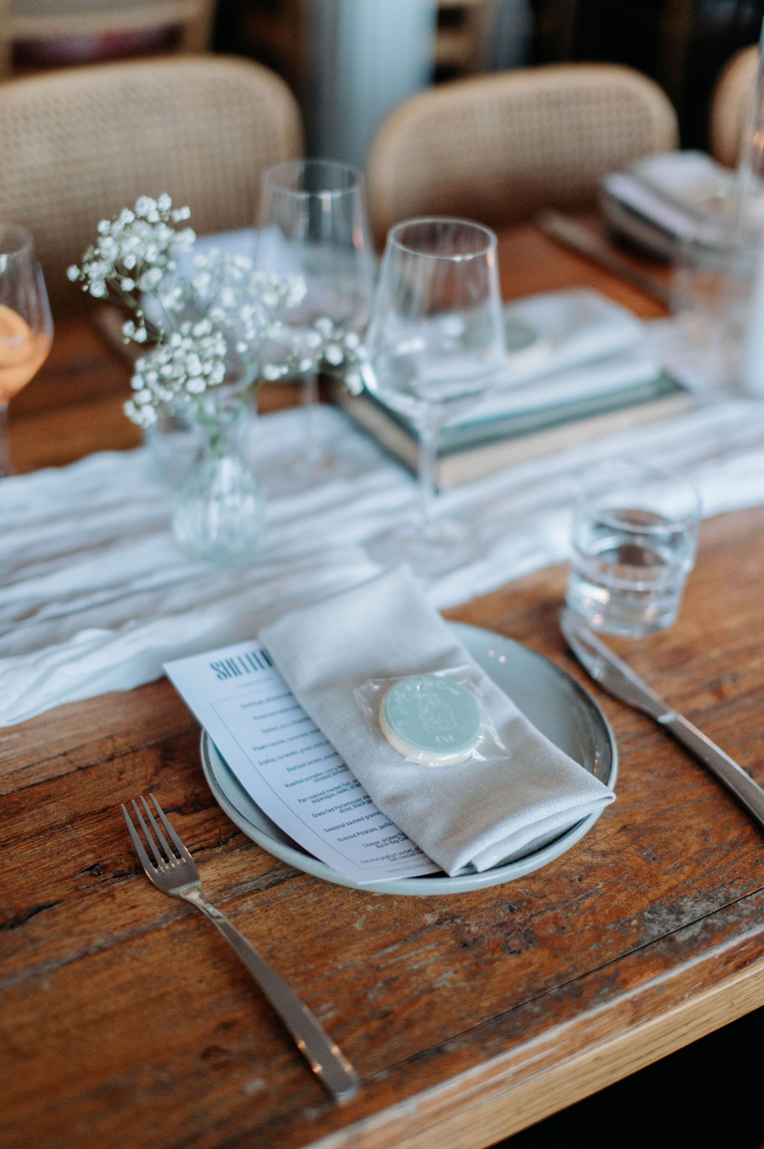 Elegant table setting with baby's breath flowers, wine glasses, and menu card on rustic wooden surface.