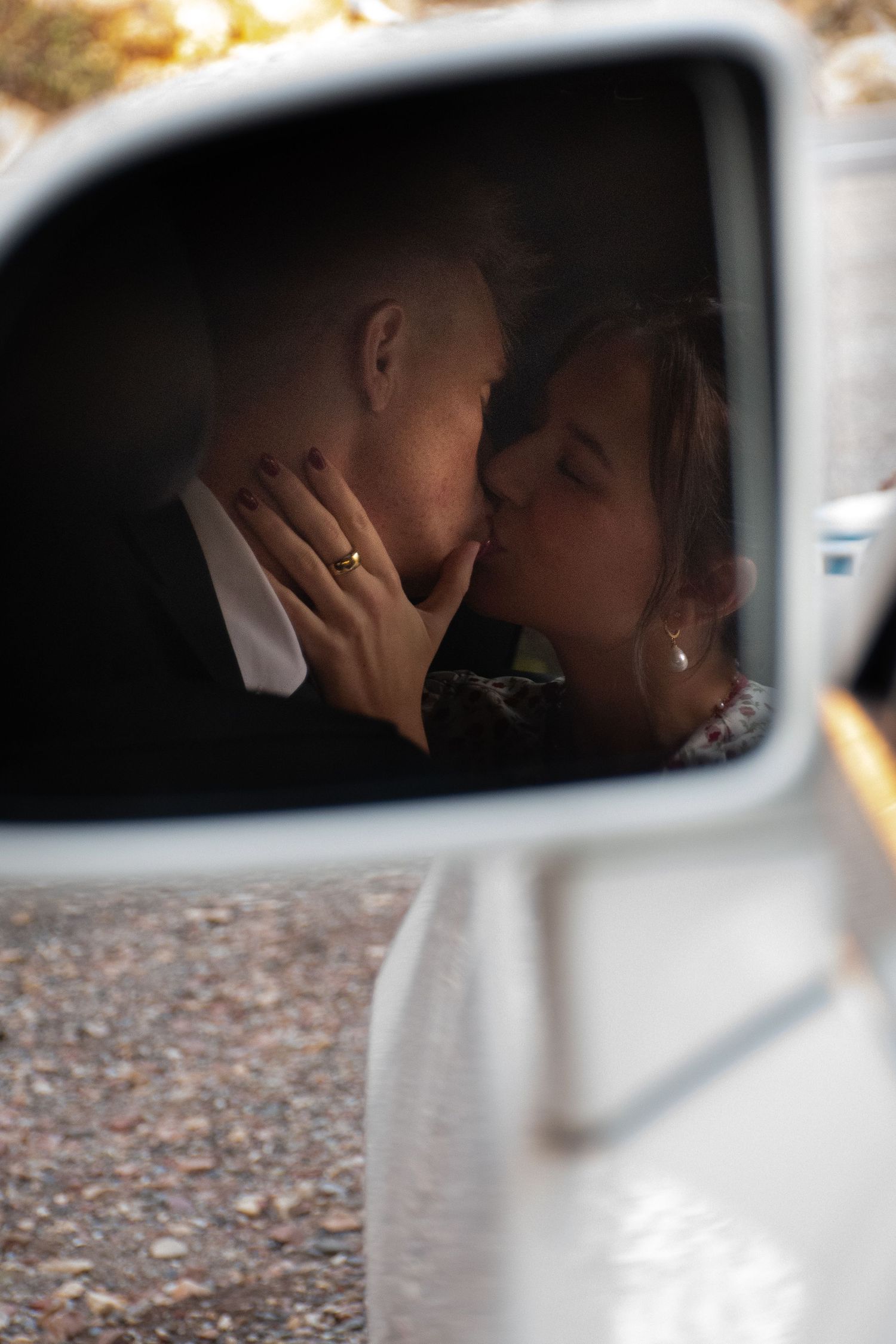 A romantic moment captured in a car's side mirror reflection showing a tender kiss between a couple.