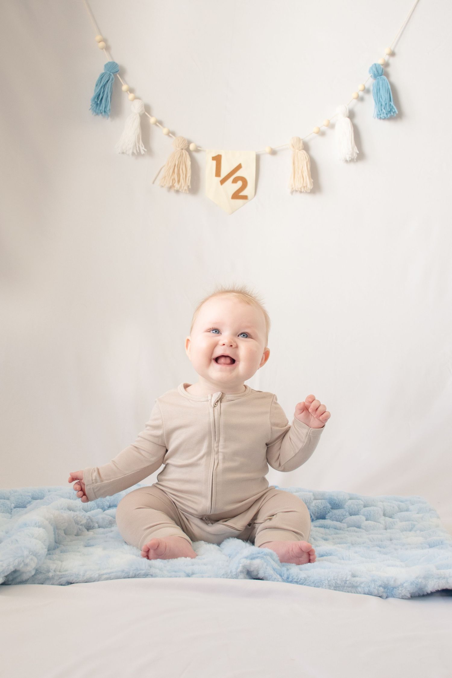 A happy baby poses for photo and sits under a decorative tassel banner with blue and cream accents in Mesa, Arizona.