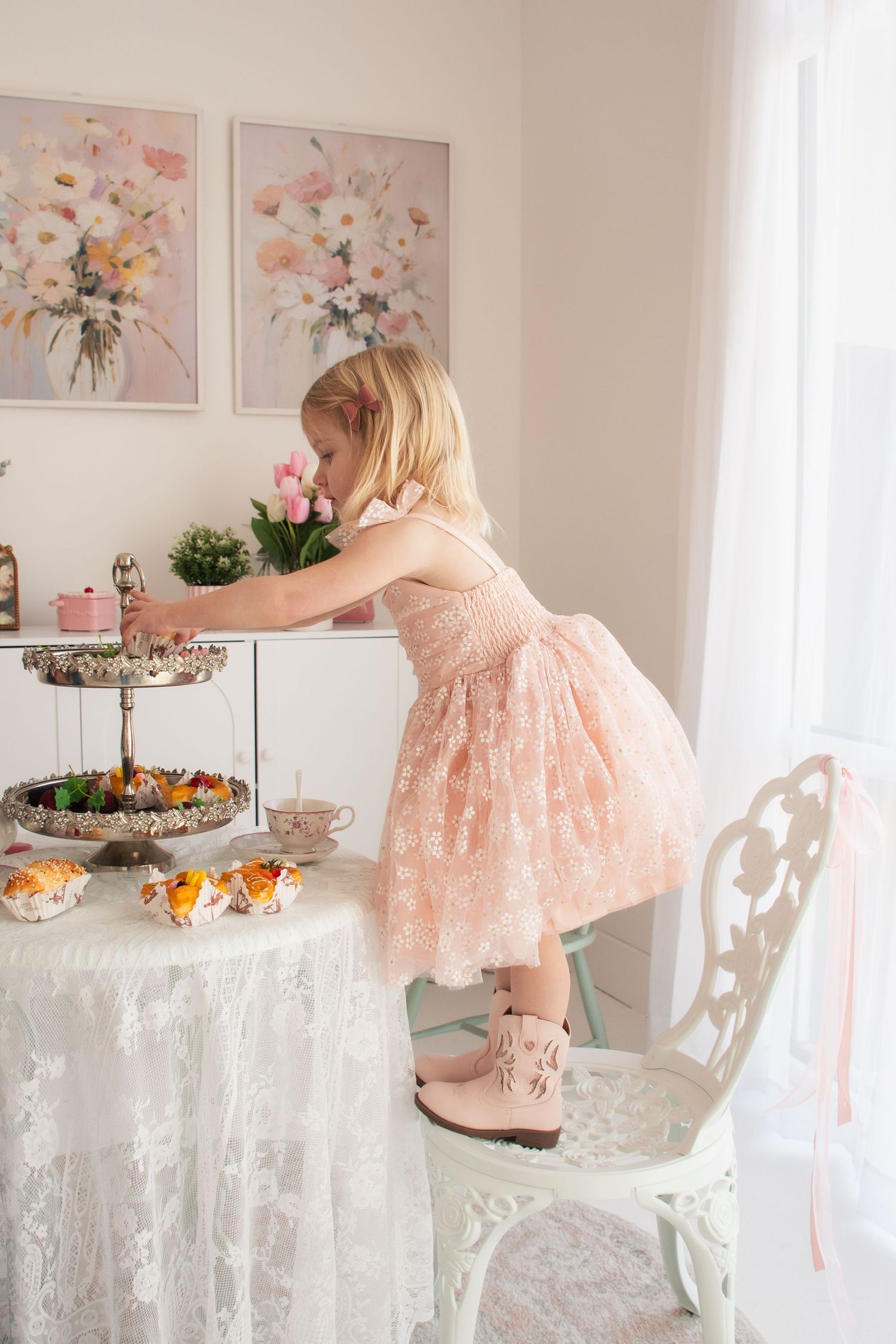 A pink lace dress and boots complement the elegant tea party setup with floral artwork and white lace tablecloth in a studio in Layton Utah.