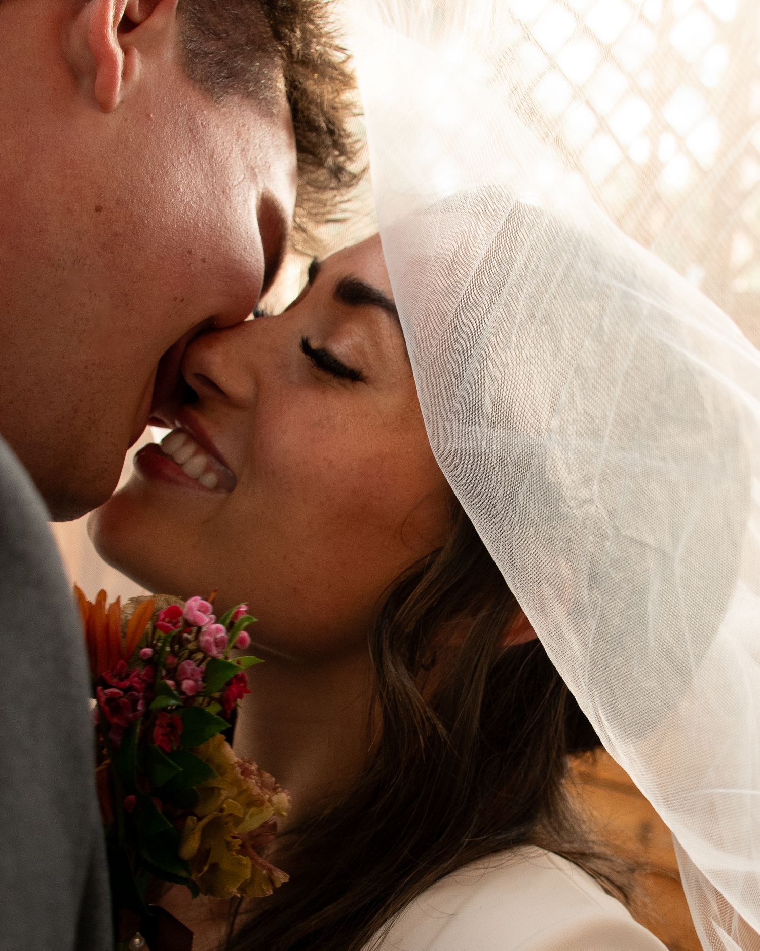 A romantic wedding moment captured in warm light with a bride in white veil and colorful floral bouquet.