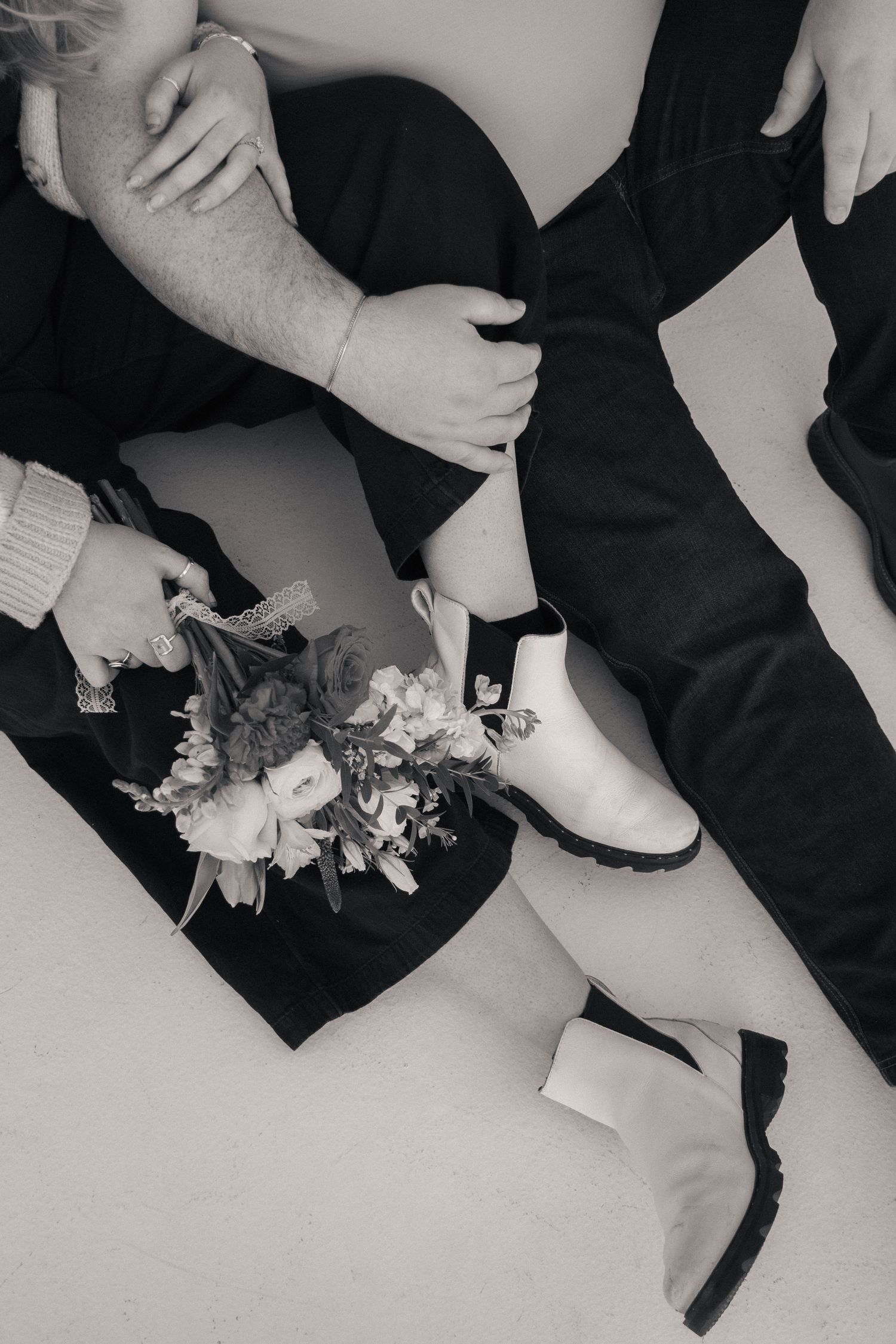 Black and white photo of formal dress shoes and a floral corsage on the floor, capturing a cozy moment between a couple.