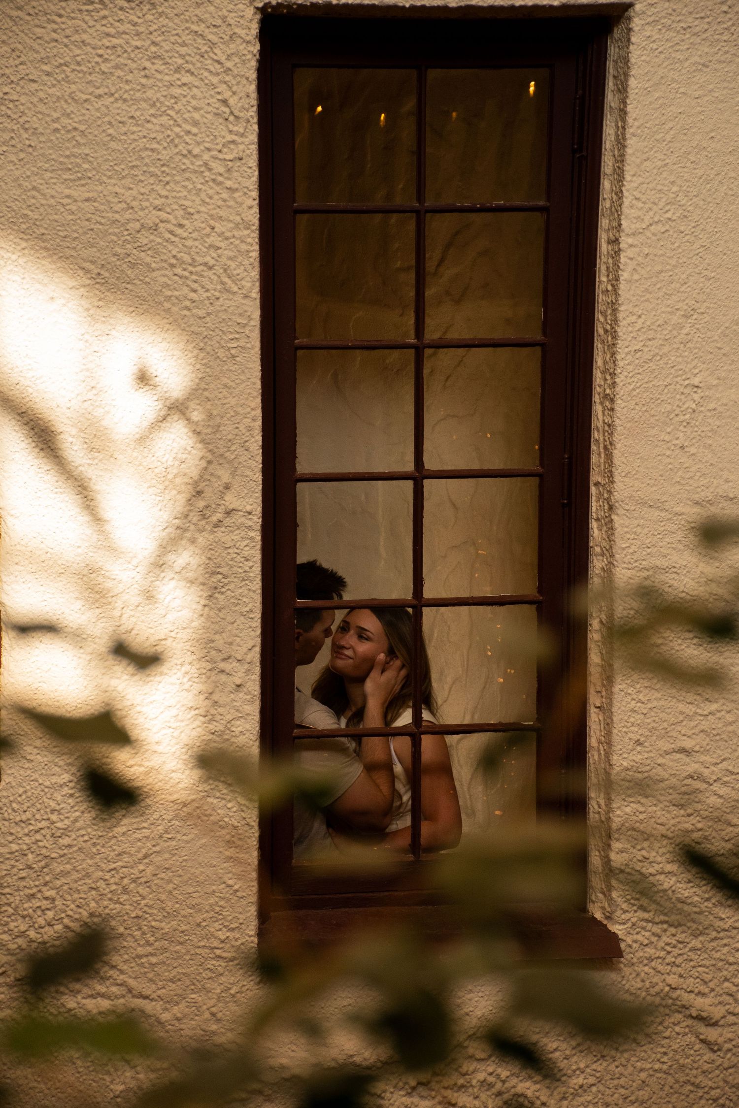 A sepia-toned triptych shows a person silhouetted in a window frame with shadows of tree branches on the wall.