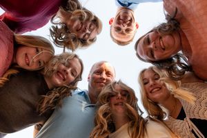 A group forms a circle looking down at the camera with bright smiles against a blue sky in American Fork Utah.