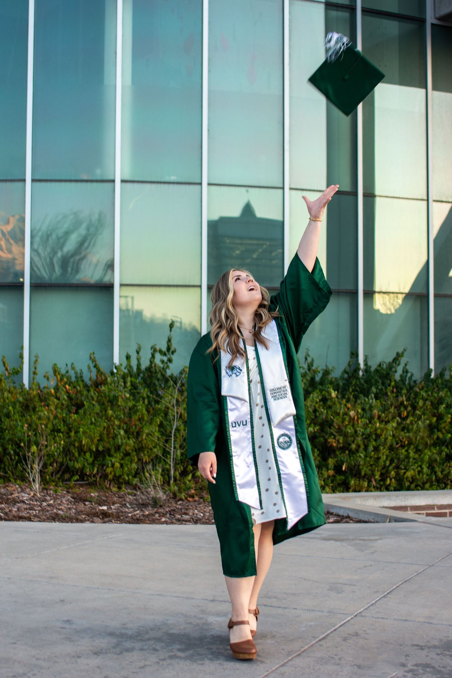 UVU student wearing gown throws cap in air.
